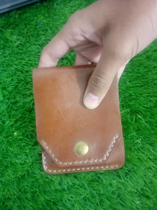 Hand holding brown handmade leather snap wallet in palm outdoors
